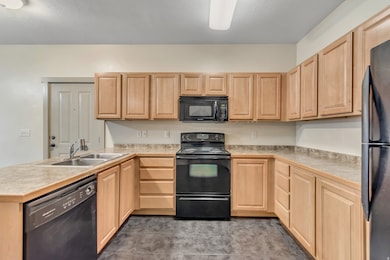 Kitchen with black appliances, light countertops, light brown cabinetry, and a peninsula