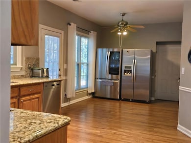 Kitchen featuring stainless steel appliances, brown cabinetry, light wood-style flooring, a ceiling fan, and light stone counters