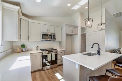 Kitchen featuring lofted ceiling, stainless steel appliances, a center island with sink, a kitchen bar, and decorative light fixtures