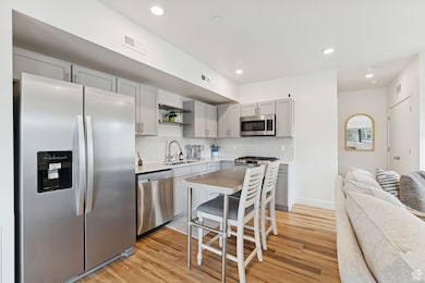 Kitchen featuring appliances with stainless steel finishes, gray cabinetry, open shelves, decorative backsplash, and light wood-style floors