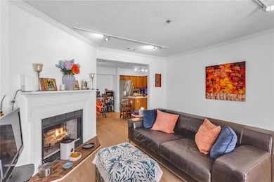 Living room featuring ornamental molding, light wood-style floors, a textured ceiling, and a lit fireplace