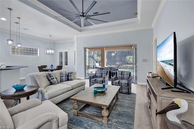 Living room featuring a raised ceiling, ornamental molding, new light vinyl planked flooring and new ceiling fan.