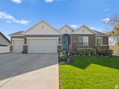 View of front facade featuring board and batten siding, a front yard, concrete driveway, a garage, and brick siding