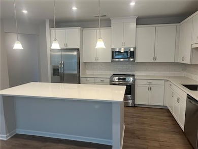 Kitchen with white cabinets, appliances with stainless steel finishes, a kitchen island, dark wood-style floors, and tasteful backsplash