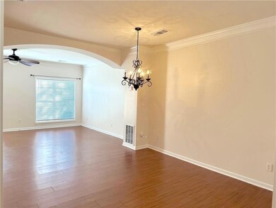 Empty room featuring arched walkways, dark wood-style flooring, ceiling fan, ornamental molding, and a chandelier