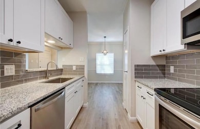 Kitchen with white cabinetry, light stone counter