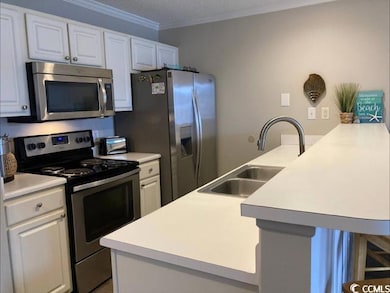 Kitchen featuring appliances with stainless steel finishes, light countertops, white cabinets, ornamental molding, and a kitchen bar