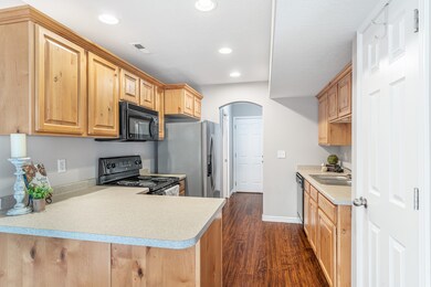 Kitchen with dark wood-style floors, black appliances, light countertops, arched walkways, and a peninsula