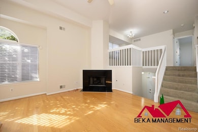 Unfurnished living room featuring stairs, a tiled fireplace, wood finished floors, and a ceiling fan