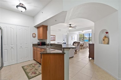 Kitchen with a peninsula, brown cabinetry, light tile patterned flooring, dark stone countertops, and a ceiling fan