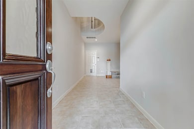 Step inside to a bright and open tiled foyer that instantly feels expansive thanks to a soaring two-story ceiling and curved architectural cutout above. This space introduces the home’s graceful flow and neutral palette. A carpeted staircase with wood rail accents curves up to the main living areas, inviting exploration of the home’s elegant, functional layout.