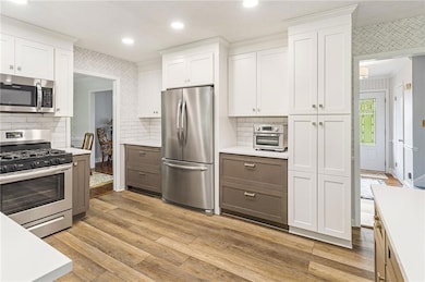 Kitchen with white cabinets, stainless steel appliances, tasteful backsplash, light wood-style floors, and recessed lighting