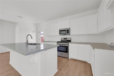 Kitchen featuring appliances with stainless steel finishes, light wood-style floors, a center island with sink, and light stone countertops