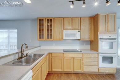 Kitchen featuring white appliances, light brown cabinetry, light wood-style flooring, and glass insert cabinets