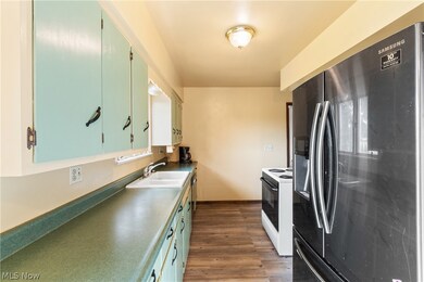Kitchen featuring black fridge with ice dispenser, wood-type flooring, sink, and white range with electric stovetop