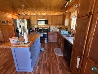 Kitchen with appliances with stainless steel finishes, wooden ceiling, dark wood-style floors, wooden walls, and brown cabinetry