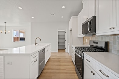Kitchen featuring appliances with stainless steel finishes, white cabinetry, decorative backsplash, light wood-style flooring, and recessed lighting