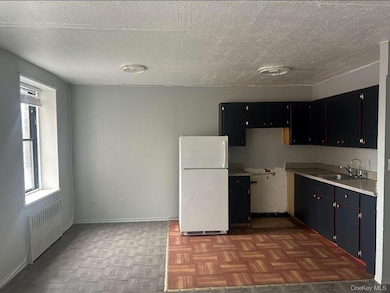 Kitchen with radiator, freestanding refrigerator, a textured ceiling, dark cabinets, and light countertops