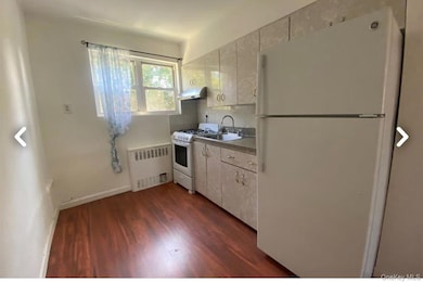 Kitchen with white appliances, radiator heating unit, dark wood-type flooring, and white cabinets