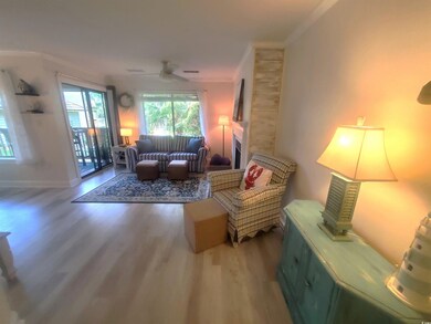 Living area with crown molding, wood finished floors, a fireplace with raised hearth, and a ceiling fan