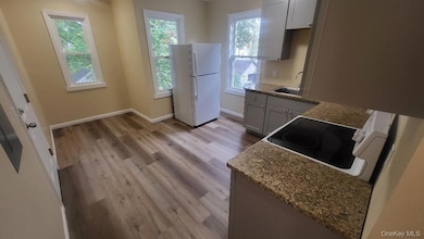 Kitchen featuring white appliances, light stone counters, light wood-type flooring, and gray cabinets