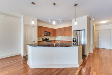 Kitchen with dark stone countertops, hanging light fixtures, decorative backsplash, brown cabinetry, and appliances with stainless steel finishes