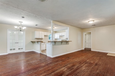 Unfurnished living room with a textured ceiling, a chandelier, dark wood-type flooring, and french doors