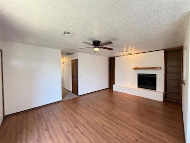 Unfurnished living room with a ceiling fan, wood finished floors, a brick fireplace, and a textured ceiling