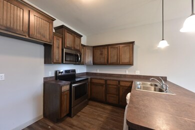 Kitchen with appliances with stainless steel finishes, dark countertops, decorative light fixtures, a peninsula, and dark wood-style floors