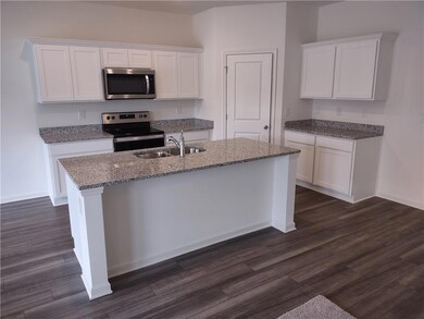 Kitchen with stainless steel appliances, white cabinets, and light stone countertops