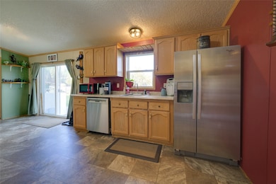 Kitchen with appliances with stainless steel finishes, light countertops, ornamental molding, a textured ceiling, and dark stone finish floors