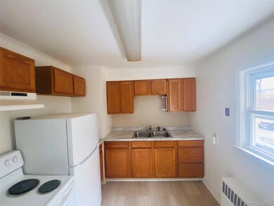 Kitchen with white electric range oven, brown cabinetry, light countertops, light wood-style floors, and under cabinet range hood