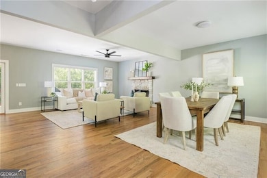 Dining room featuring a stone fireplace, a ceiling fan, baseboards, and light wood-style flooring