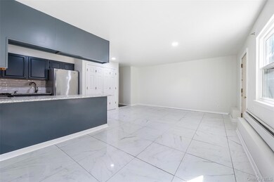 Kitchen featuring light marble finish floors, light stone countertops, freestanding refrigerator, backsplash, and a baseboard heating unit