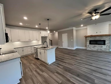 Kitchen with appliances with stainless steel finishes, island with single bowl ss sink, granite counter tops, white cabinetry, decorative backsplash, traverse lights, and trash can pull cabinet.