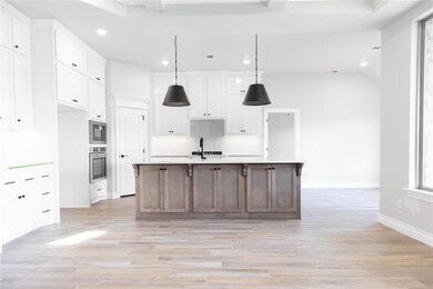 Kitchen with white cabinets, decorative light fixtures, a center island with sink, light wood-style flooring, and recessed lighting