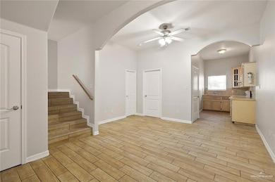 Unfurnished living room with ceiling fan, light wood-type flooring, arched walkways, and stairs