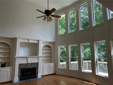 Unfurnished living room with built in shelves, a ceiling fan, wood finished floors, healthy amount of natural light, and a towering ceiling