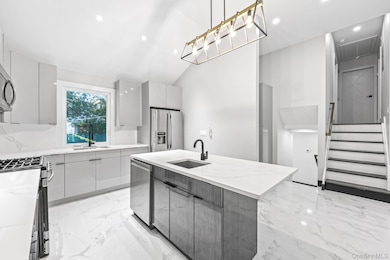 Kitchen with an island with sink, light marble finish floors, appliances with stainless steel finishes, modern cabinets, and light stone counters