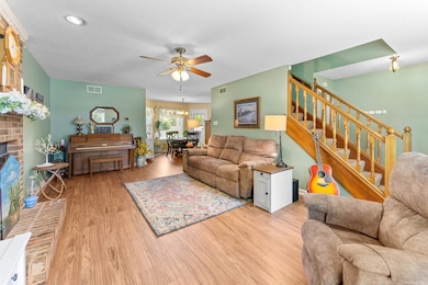 Living area with a ceiling fan, wood finished floors, a textured ceiling, a brick fireplace, and stairs