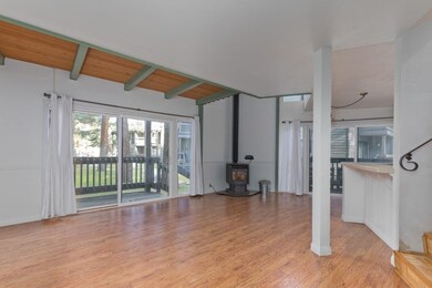 Unfurnished living room with a wood stove, light wood-style flooring, beamed ceiling, and healthy amount of natural light