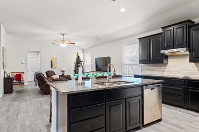 Kitchen with dark cabinets, light wood-style flooring, light stone counters, decorative backsplash, and vaulted ceiling
