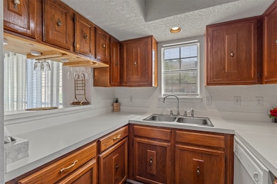 Kitchen with brown cabinets, light countertops, white dishwasher, a textured ceiling, and recessed lighting
