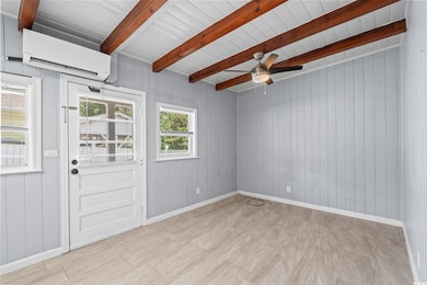 Empty room with a wall mounted AC, beam ceiling, wood walls, and a ceiling fan