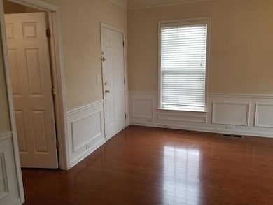 Empty room featuring dark wood-type flooring, a decorative wall, ornamental molding, and wainscoting