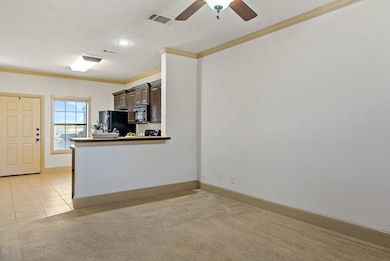Kitchen with crown molding, light tile patterned flooring, light carpet, black appliances, and dark brown cabinets