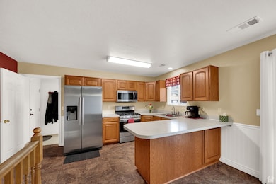 Kitchen featuring appliances with stainless steel finishes, light countertops, a wainscoted wall, a peninsula, and brown cabinets