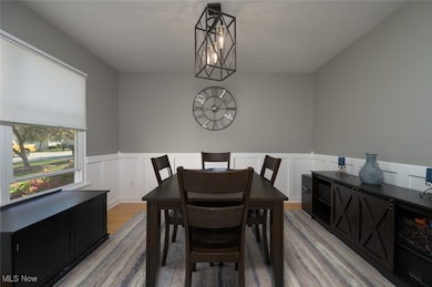 Dining area with light wood-style floors, wainscoting, a decorative wall, a textured ceiling, and a chandelier