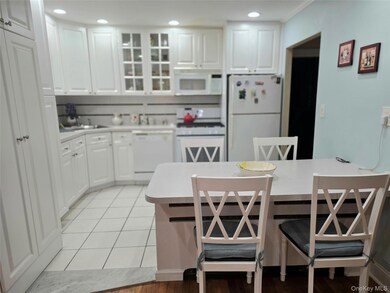 Kitchen with a breakfast bar, white appliances, light countertops, glass insert cabinets, and recessed lighting