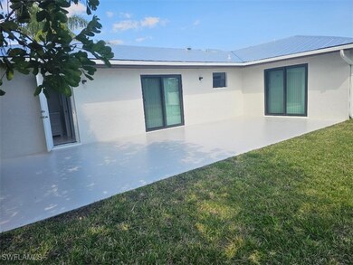 Rear view of house with stucco siding, a lawn, metal roof, and a patio area
